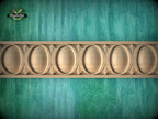 a close-up view of a wooden carving with a repeating pattern of oval shapes, set against a green textured background.