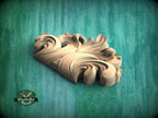 A wooden carving of a stylized leaf or flower design is displayed against a green background.