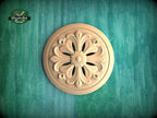 A wooden ornamental piece with a floral design is displayed against a green textured background.
