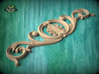 A decorative wooden carving with intricate scrollwork and floral elements is displayed against a teal background.