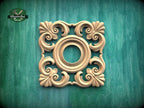 a square, ornate wooden carving with a central circular opening, set against a green wooden background.