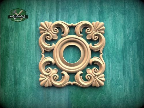 a square, ornate wooden carving with a central circular opening, set against a green wooden background.
