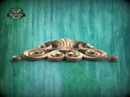 A decorative wooden carving with intricate swirls and curves is displayed against a teal-colored background.