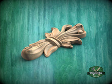 Load image into Gallery viewer, A wooden carving of a stylized flower or leaf design is displayed against a green background.

