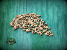 Load image into Gallery viewer, an ornate, carved wooden piece with intricate scrollwork and floral designs, set against a green wooden background.
