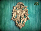 an ornate, carved wooden panel with intricate floral and leaf designs, set against a green background.