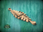 A wooden carving of a leaf-like design is displayed against a green background.
