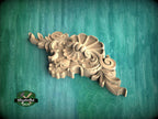 A carved wooden ornament with intricate floral and scroll designs is displayed against a green background.