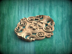 A decorative wooden carving with intricate swirls and curves is displayed against a green background.