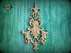 an ornate, carved wooden piece with intricate, decorative elements, such as leaves and flowers, mounted on a green wooden background.