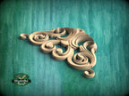 A decorative wooden carving in the shape of a flower or scroll design is displayed against a teal background.