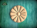 a wooden flower-shaped object with a round center and petals arranged in a circular pattern, set against a green background.