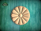a wooden flower-shaped object with a round center and petals arranged in a circular pattern, set against a green background.