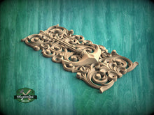 Load image into Gallery viewer, A decorative wooden carving with intricate swirls and patterns is displayed against a green background.
