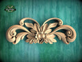 A decorative wooden carving with intricate floral and leaf designs is displayed against a green textured background.
