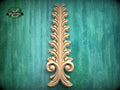 a decorative wooden leaf-like object with a vertical, ornate design on a green background.