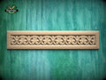A decorative wooden panel with an intricate floral design is displayed against a green textured background.