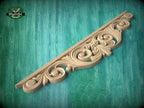 A decorative wooden carving with intricate scrollwork is displayed against a teal background.