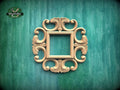 a decorative wooden frame with an ornate, floral design, mounted on a green wooden surface.
