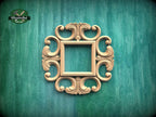 a decorative wooden frame with an ornate, floral design, mounted on a green wooden surface.