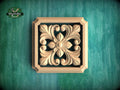 a square wooden carving with an intricate floral design, set against a green background.