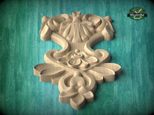 Load image into Gallery viewer, A carved wooden design with intricate floral and leaf-like patterns, set against a green background.
