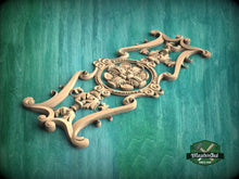 Load image into Gallery viewer, A decorative wooden carving with intricate floral and scrollwork designs is displayed against a green background.
