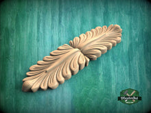 Load image into Gallery viewer, A wooden carving of a leaf-like design is displayed against a green background.
