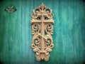 a decorative wooden cross with intricate carvings and scrollwork, mounted on a green wooden surface.