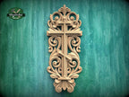 a decorative wooden cross with intricate carvings and scrollwork, mounted on a green wooden surface.