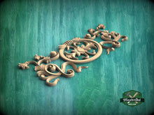 Load image into Gallery viewer, A decorative wooden carving with intricate floral and scrollwork designs is displayed against a green textured background.

