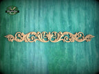 A decorative wooden carving with an intricate floral design is displayed against a textured green background.
