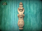 a wooden carving of a decorative finial or finial-like object, which is mounted on a green wooden surface.