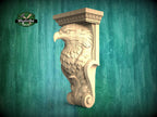 A carved wooden eagle figure is displayed against a teal background, with a logo and text visible in the top left corner.