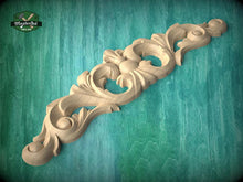 Load image into Gallery viewer, A decorative wooden carving with intricate floral and scrollwork designs is displayed against a teal background.
