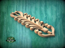 Load image into Gallery viewer, A decorative wooden leaf-like object with intricate patterns and designs, resting on a green textured background.
