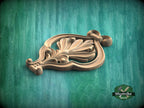A wooden carving of a stylized flower or plant design is displayed against a green background.