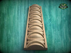A wooden carving with a series of curved shapes arranged in a vertical line, set against a green background.