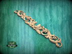 A decorative wooden carving with intricate floral and scroll designs is displayed against a green textured background.