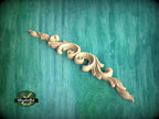 A decorative wooden carving with a scroll-like design is displayed against a teal-colored background.
