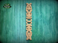 A decorative wooden carving in the shape of a vertical column with intricate scrollwork is displayed against a green textured background.