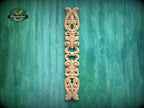 A decorative wooden carving in the shape of a vertical column with intricate scrollwork is displayed against a green textured background.