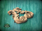 A decorative wooden carving in the shape of a stylized flower or leaf, with intricate swirls and curves, is displayed against a green background.