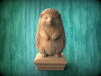 A wooden hedgehog statue is displayed on a wooden pedestal against a green background.