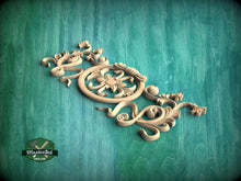 Load image into Gallery viewer, A decorative wooden carving with intricate floral and scrollwork designs is displayed against a green wooden background.
