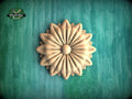 A wooden flower-shaped object is displayed against a green background.
