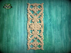 an ornate, carved wooden panel with intricate floral and scroll designs, mounted on a green wooden surface.
