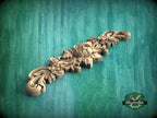 A decorative wooden carving with intricate floral and leaf designs is displayed against a green background.