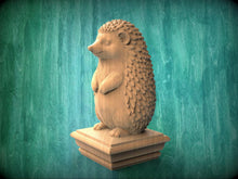 Load image into Gallery viewer, A wooden sculpture of a hedgehog standing on a pedestal against a green background.
