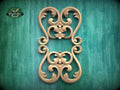 a decorative wooden carving with intricate scrollwork and floral designs, set against a green background.
